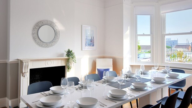 A dining room with a long table set for a meal, a fireplace, and a large window with a view. - 7 Seafield Road (Seaton)