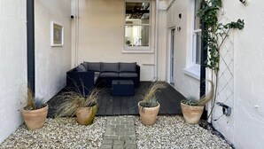 A covered patio area with a black wooden pergola, a black sofa, and three terracotta planters with plants. - 7 Seafield Road (Seaton)
