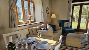 A cozy living room with a wooden table set for dining, a sofa, and a chair. - The Cider House (Axminster)