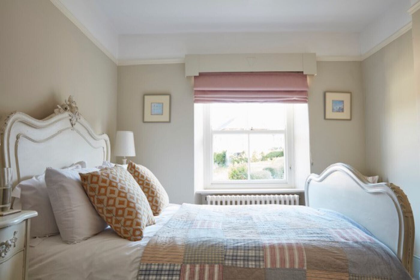 Un dormitorio con cama, mesita de noche, ventana con vistas y dos cuadros en la pared.