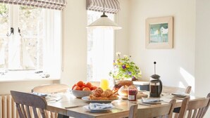 A dining area with a wooden table set for breakfast, including croissants, oranges, and a coffee pot. - Lavender Cottage (Seaton)