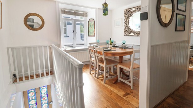 A dining area with a wooden table and chairs, a window with blinds, and a decorative mirror on the wall. - Coombe Street Cottage (Lyme Regis)