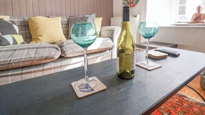 A living room with a sofa, a table with a wine bottle and glasses, and decorative plates on the wall. - Coombe Street Cottage (Lyme Regis)