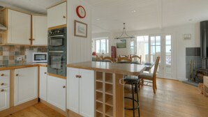 A spacious kitchen with white cabinetry, a wooden island, and a dining area with a view. - Dolphins Leap (Bridport)