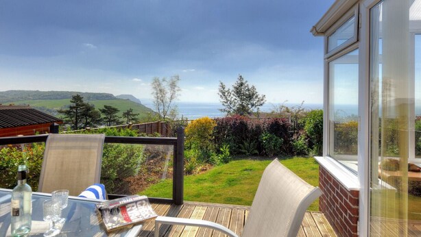 A terrace with a table, chairs, and a view of the sea and hills. - Dolphins Leap (Bridport)
