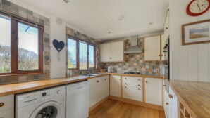 A compact kitchen with a washing machine, wooden countertops, and a tiled backsplash. - Dolphins Leap (Bridport)