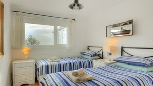 A bedroom with two beds, white nightstands, a window with curtains, a ceiling light, and a framed picture on the wall. - Dolphins Leap (Bridport)
