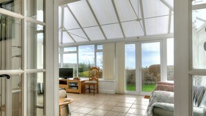 A conservatory with a TV, wooden furniture, and a view of the outdoors. - Dolphins Leap (Bridport)