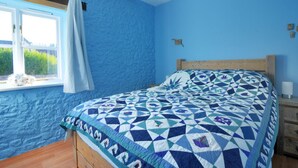 A bedroom with a blue wall, a wooden bed frame, and a patterned bedspread. - 2 Home Farm South (Lyme Regis)