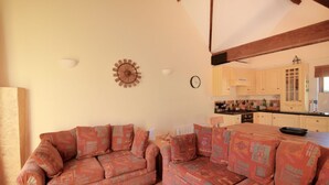 A cozy living room with a sofa and a dining table, a kitchen with wooden cabinets, and a clock on the wall. - 2 Home Farm South (Lyme Regis)