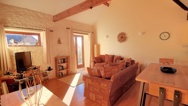 A cozy living room with a sofa, a television, a bookshelf, and a dining table. - 2 Home Farm South (Lyme Regis)