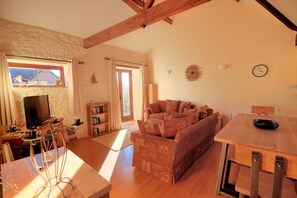 A cozy living room with a sofa, a television, a bookshelf, and a dining table. - 2 Home Farm South (Lyme Regis)