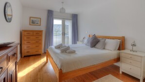 A bedroom with a wooden bed, a nightstand, a dresser, and a window with curtains. - Seashell (Lyme Regis)