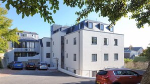 A modern building with multiple floors, a parking area with several cars, and a clear sky. - Seashell (Lyme Regis)