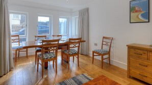 A dining area with a wooden table and chairs, a wooden dresser, and a painting of a beach scene. - Seashell (Lyme Regis)