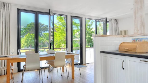 A modern kitchen with a wooden table and chairs, large windows, and a view of greenery outside. - No. 2, 26 Broad Street (Lyme Regis)