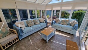 A sunlit room with two light blue sofas, a wooden coffee table, and wicker chairs. - Hove To (Lyme Regis)