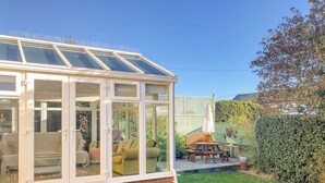 A conservatory with a glass roof, a brick base, and a patio area with outdoor furniture. - Hove To (Lyme Regis)
