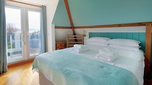 A bedroom with a bed, a wooden ladder, a nightstand, and a window with curtains. - Hove To (Lyme Regis)