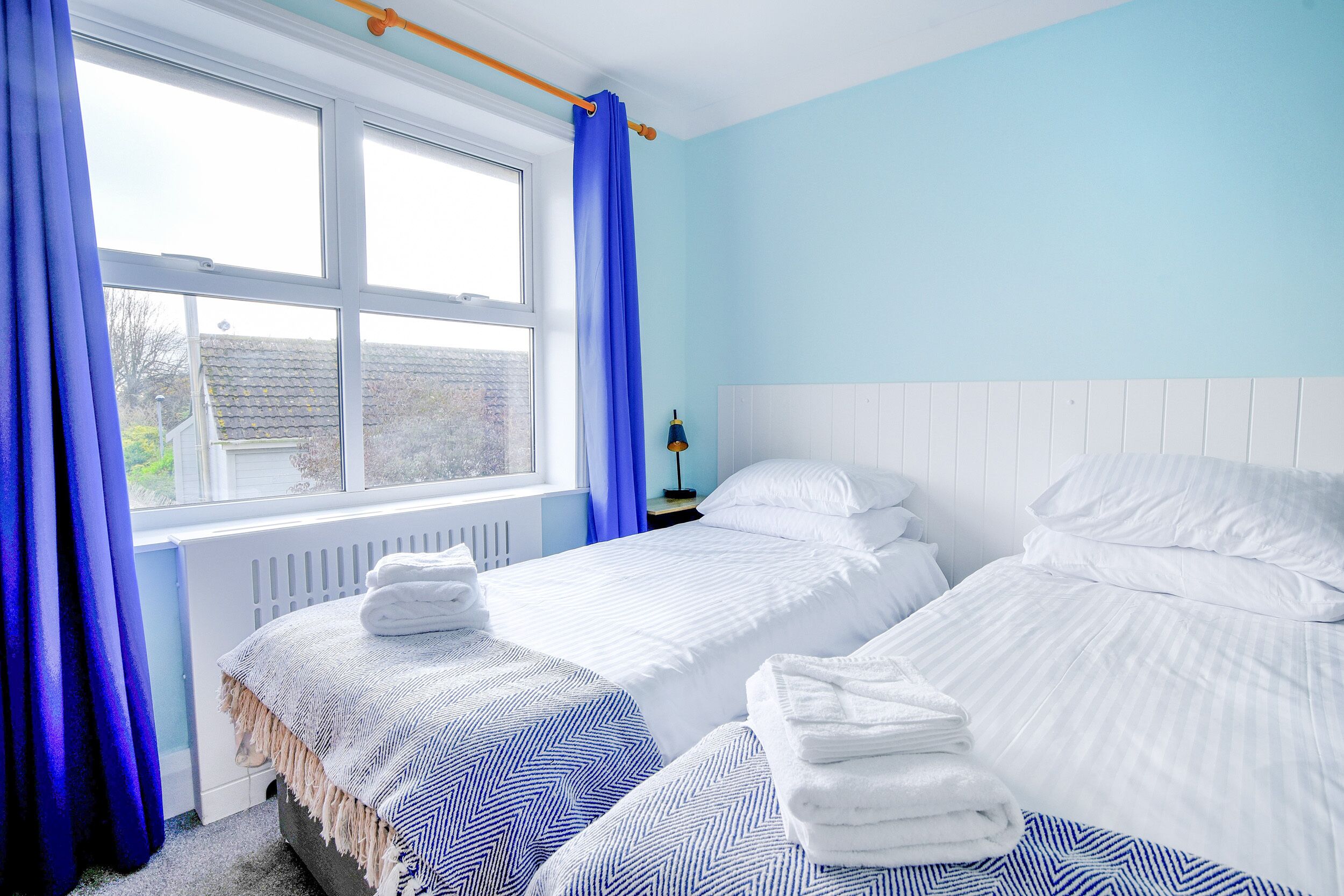 Un dormitorio con dos camas, una ventana con cortinas azules y un radiador.