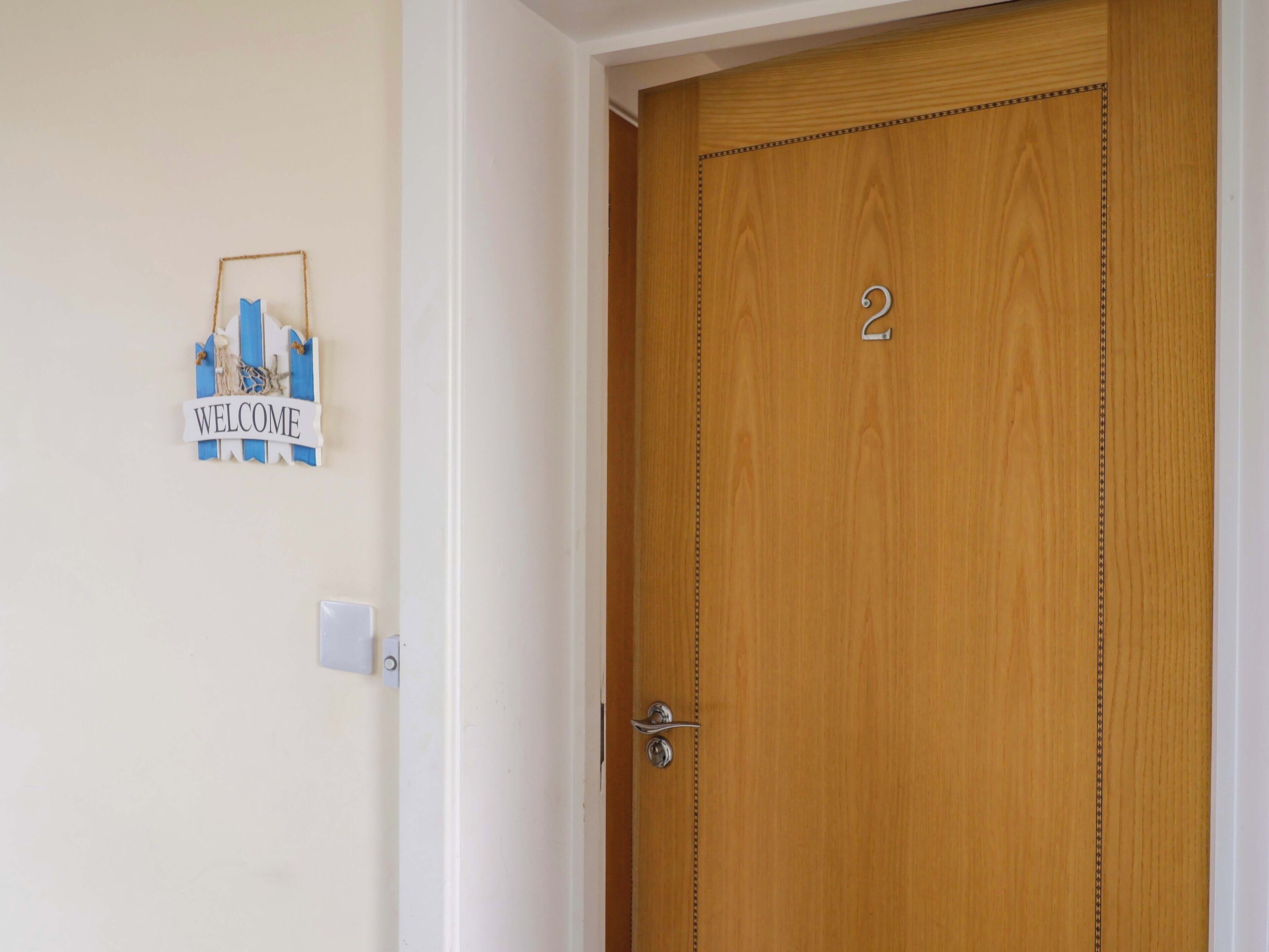 A wooden door with a number '2' and a 'WELCOME' sign on the wall.