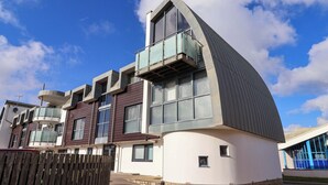 A modern building with a curved roof, large windows, and a wooden fence in the foreground. - 2 Driftwood (Bridport)