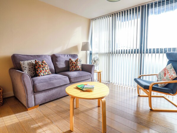 A modern living room with a grey sofa, colorful pillows, a wooden coffee table, and a blue armchair. - 2 Driftwood (Bridport)