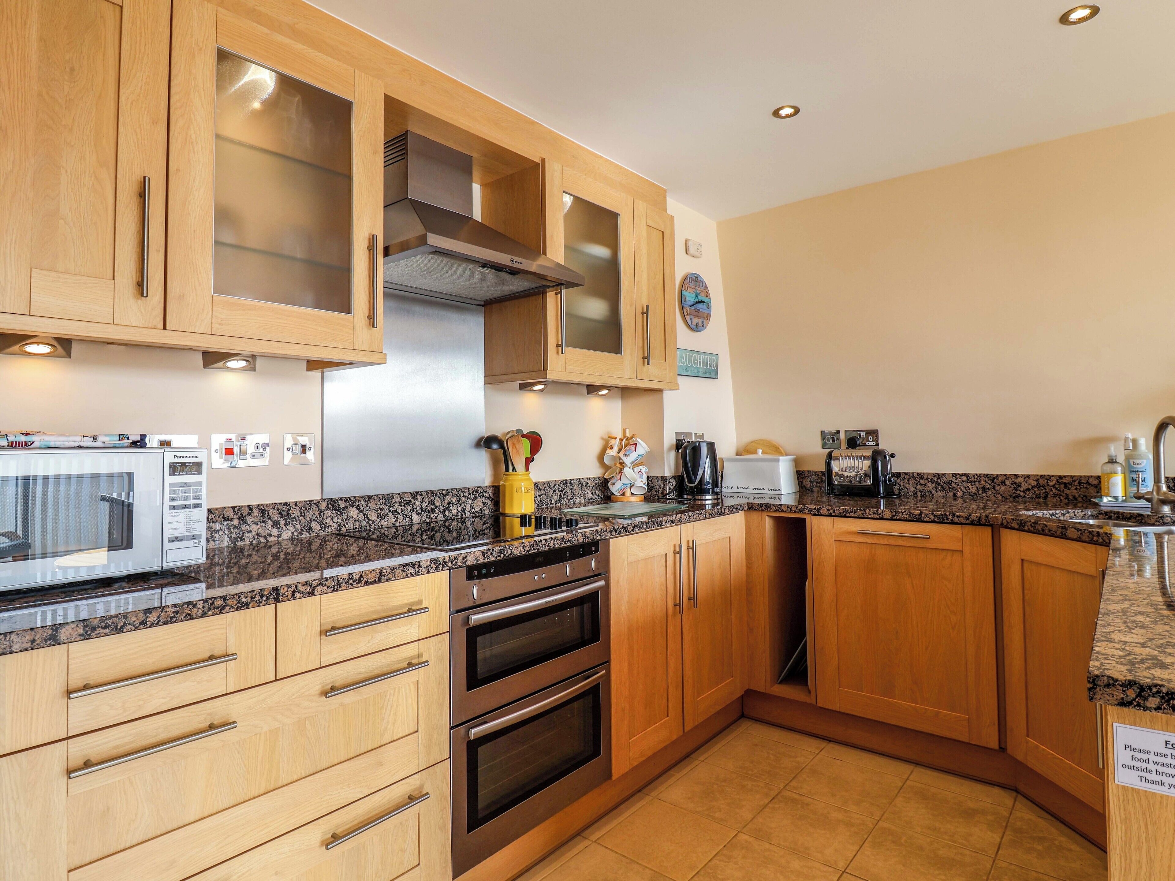 A modern kitchen with wooden cabinets, a stainless steel range hood, a microwave, an oven, and a granite countertop.