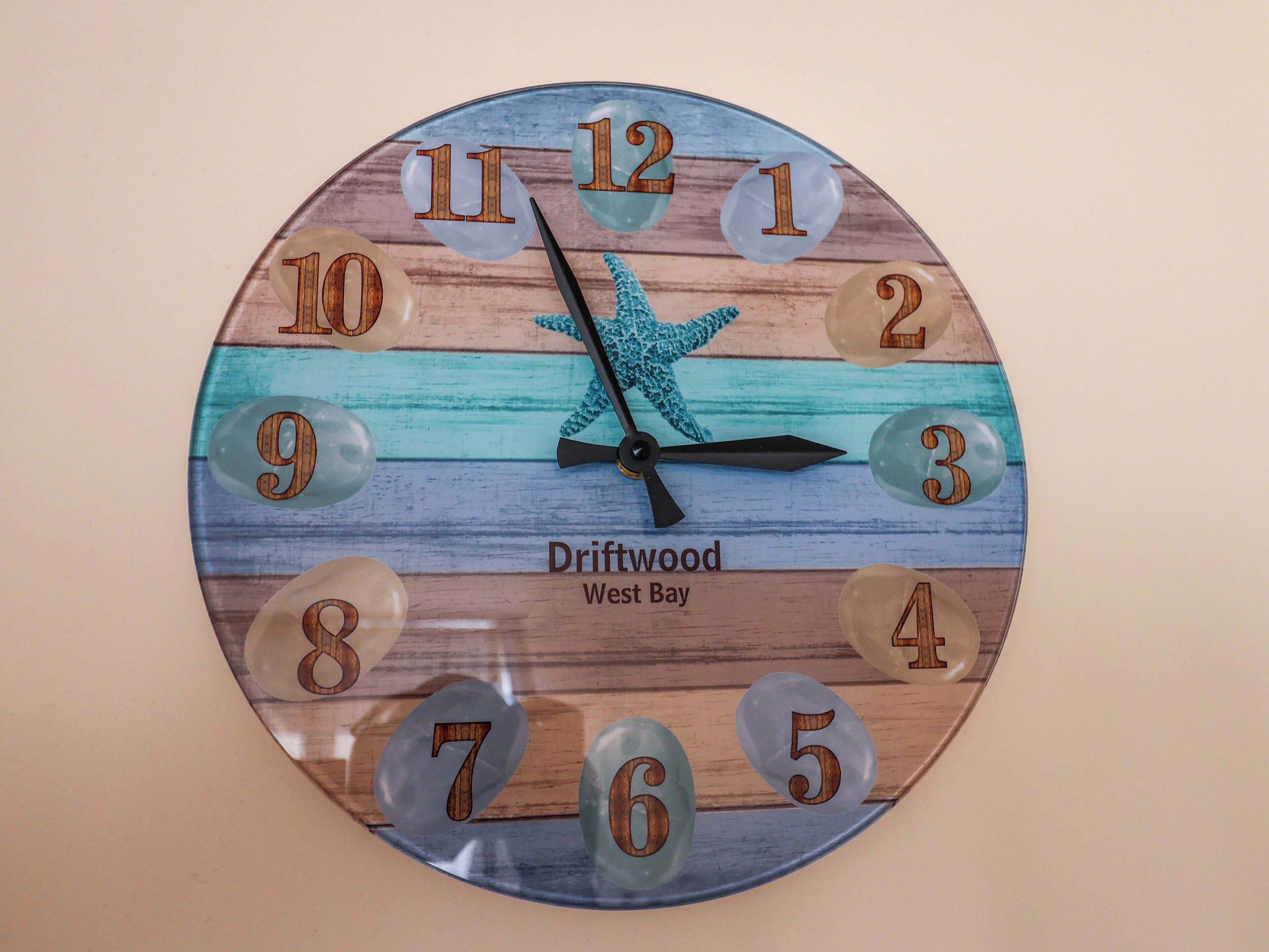 A wooden clock with a starfish decoration and the text "Driftwood West Bay" on it.