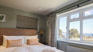 Una cama bien hecha con almohadas y toallas dobladas, una lámpara de noche, una ventana con cortinas y un radiador.