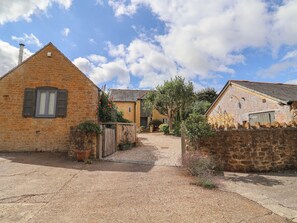 A courtyard with stone buildings, a gravel path, and a wooden fence.