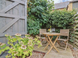 A wooden table and chairs set in a garden with a wooden fence and greenery. - The Stone Barn (Bridport)