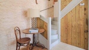 A room with a wooden staircase, a round table with a lamp, and a chair. - The Stone Barn (Bridport)