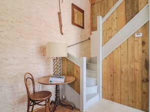 A room with a wooden staircase, a round table with a lamp, and a chair. - The Stone Barn (Bridport)