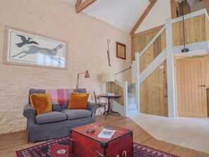 A cozy living room with a grey sofa, a red trunk, and a wooden staircase.