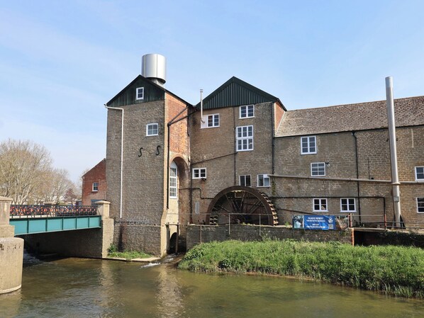 A historic building with a large water wheel, a bridge, and a river. - The Stone Barn (Bridport)