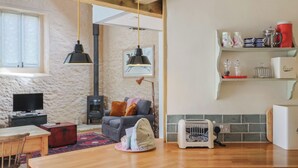 A cozy living room with a fireplace, a television, and a sofa. There's a kitchen area with a toaster and a kettle on the counter. - The Stone Barn (Bridport)