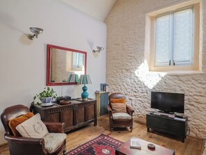 A cozy living room with a stone wall, a television, a wooden cabinet, and a comfortable chair.