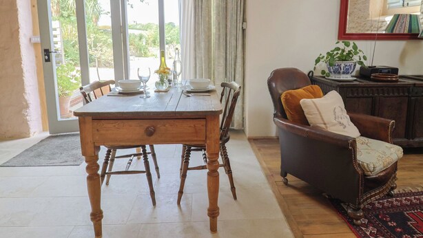 A dining area with a wooden table, chairs, and a view through a glass door to an outdoor garden. - The Stone Barn (Bridport)