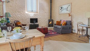 A cozy living room with a fireplace, a dining area with a table set for two, and a comfortable seating arrangement. - The Stone Barn (Bridport)