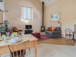 A cozy living room with a fireplace, a dining area with a table set for two, and a comfortable seating arrangement. - The Stone Barn (Bridport)