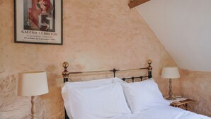 A room with a bed, two bedside tables with lamps, a poster on the wall, and a sloped ceiling. - The Stone Barn (Bridport)