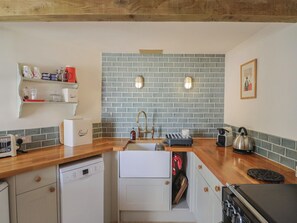 A kitchen with a brick backsplash, wooden countertops, a Bosch dishwasher, a Bosch bread maker, a kettle, and a coffee maker.