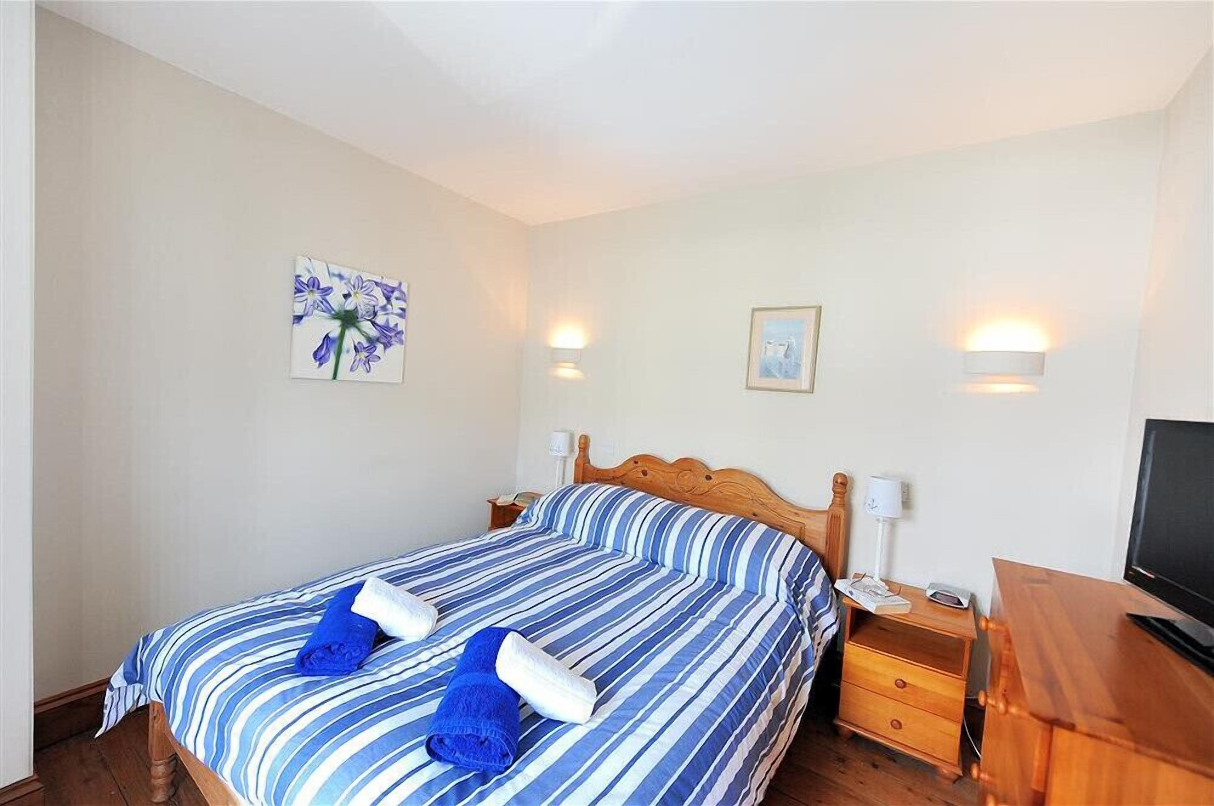 Een slaapkamer met een bed, twee nachtkastjes, een tv en wandlampen.