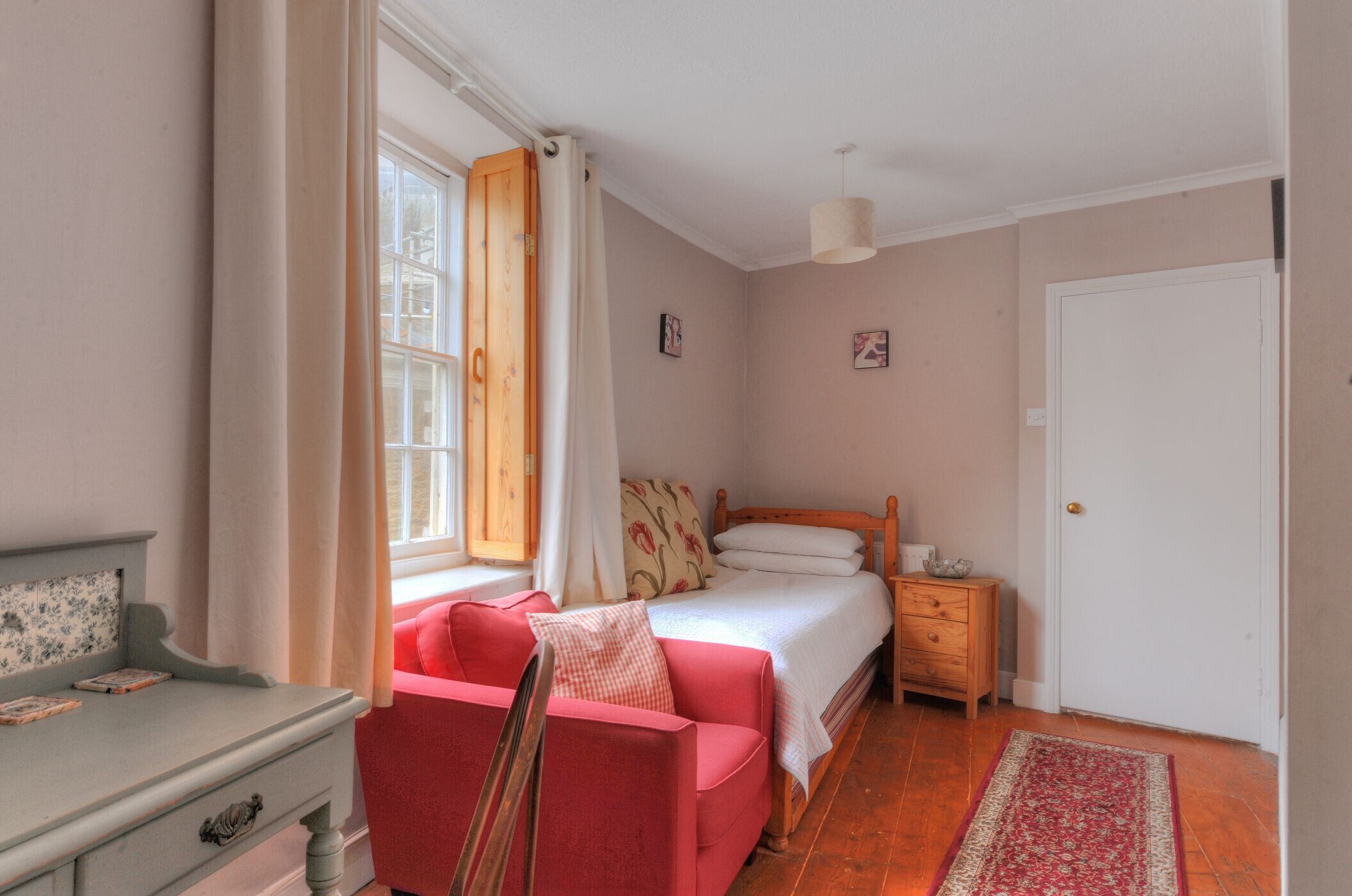 Une chambre à coucher avec un lit, une chaise rouge, une table de chevet en bois et une porte blanche.