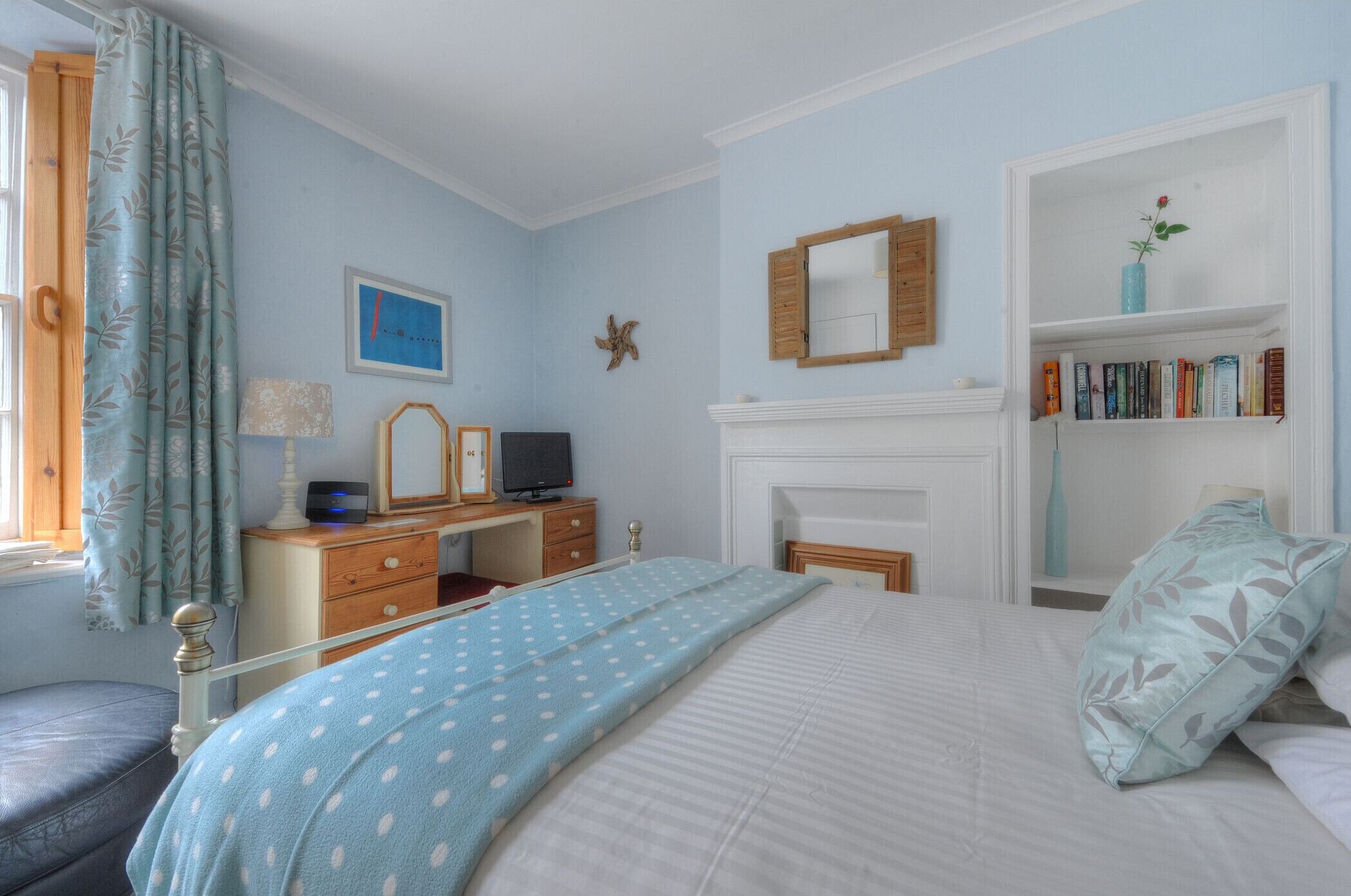 Ein Schlafzimmer mit einem Bett, einem Schminktisch, einem Fernseher, einem Bücherregal und einem Kamin.