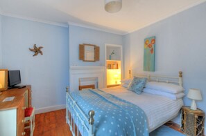 A bedroom with a bed, bedside table, lamp, and a small desk with a chair. - Driftwood (Lyme Regis)