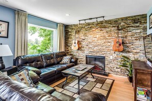 A living room with a stone wall, leather sofa, a fireplace, and a guitar. - Riverfront View near Downtown, Walk to Restaurants (Nashville)