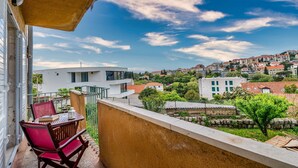 Varanda com mesa e cadeiras, vista para uma colina com edifícios e vegetação.