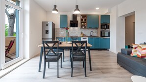 Uma cozinha moderna com armários verde-água, uma área de jantar com mesa e cadeiras, e um sofá cinzento.